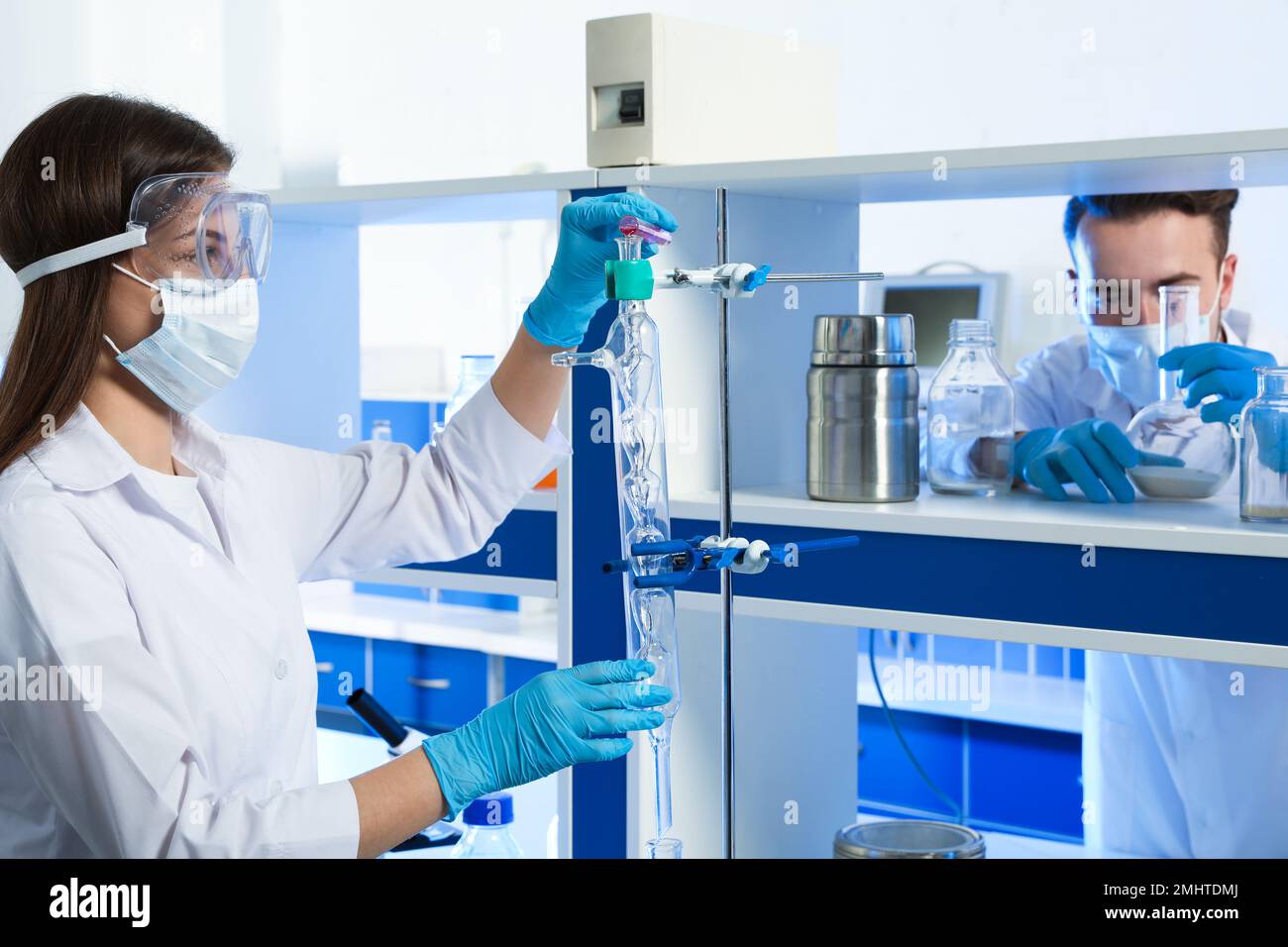 Scientist pouring liquid through glass distillation condenser indoors