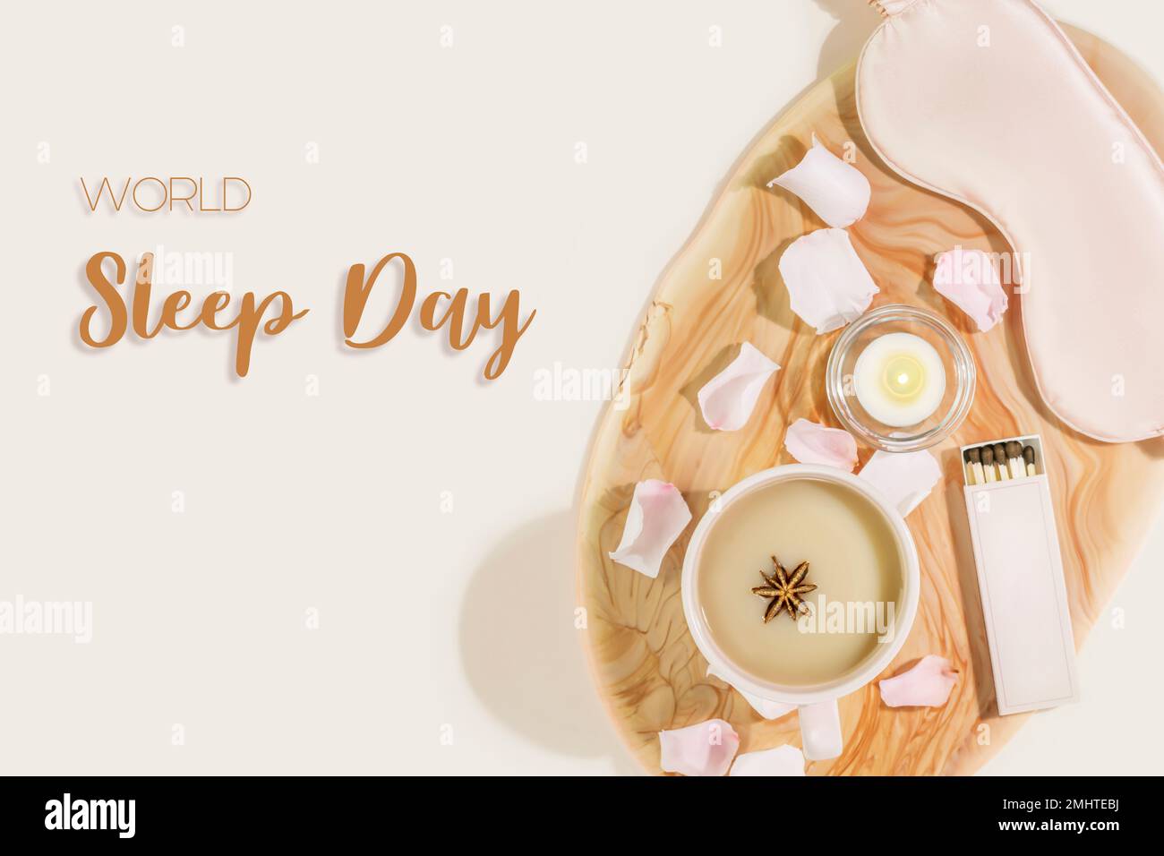 World Sleep Day card with mask for sleep, cup of tea with milk, candle and rose petals on pink marble tray on pink background with inscription World S Stock Photo