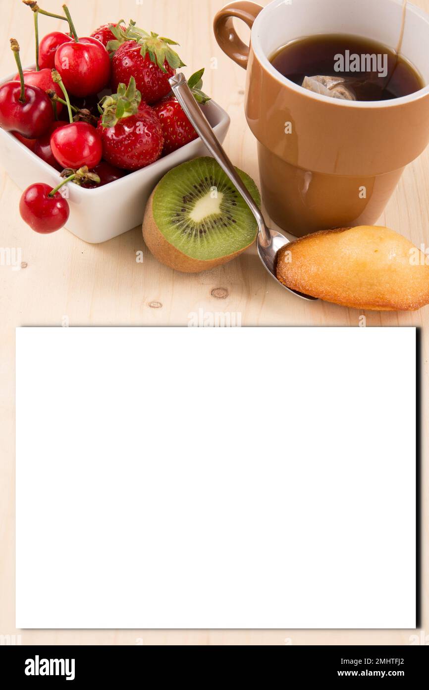 https://c8.alamy.com/comp/2MHTFJ2/cup-of-tea-with-strawberry-cherry-kiwi-and-a-madeleine-pastry-lying-on-a-wooden-table-with-blank-sheet-paper-for-text-food-mock-up-empty-white-card-pa-2MHTFJ2.jpg