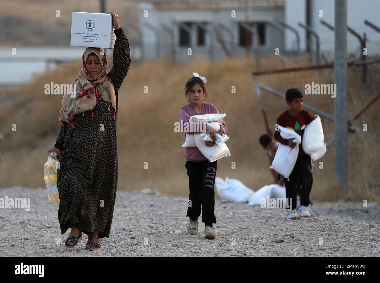 A Syrian woman and her children, who were displaced by the Turkish military  operation in northeastern Syria, carry food supplies at the Bardarash  refugee camp, north of Mosul, Iraq, Thursday, Oct. 17,