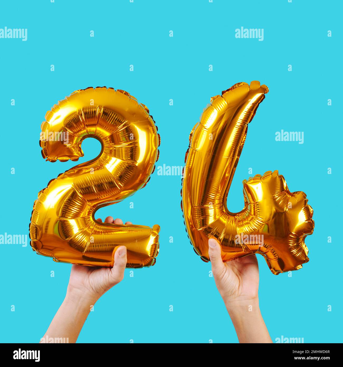 a caucasian man holds some golden number-shaped balloons forming the number 24 on a blue background Stock Photo