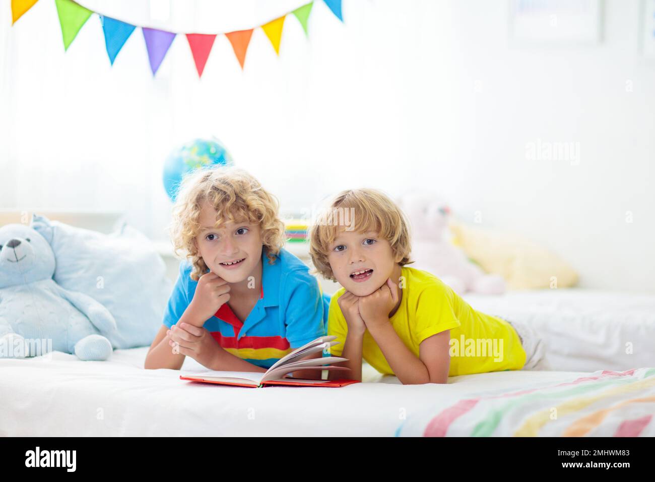 Child reading book in bed. Bedroom for two kids. Little boys read books