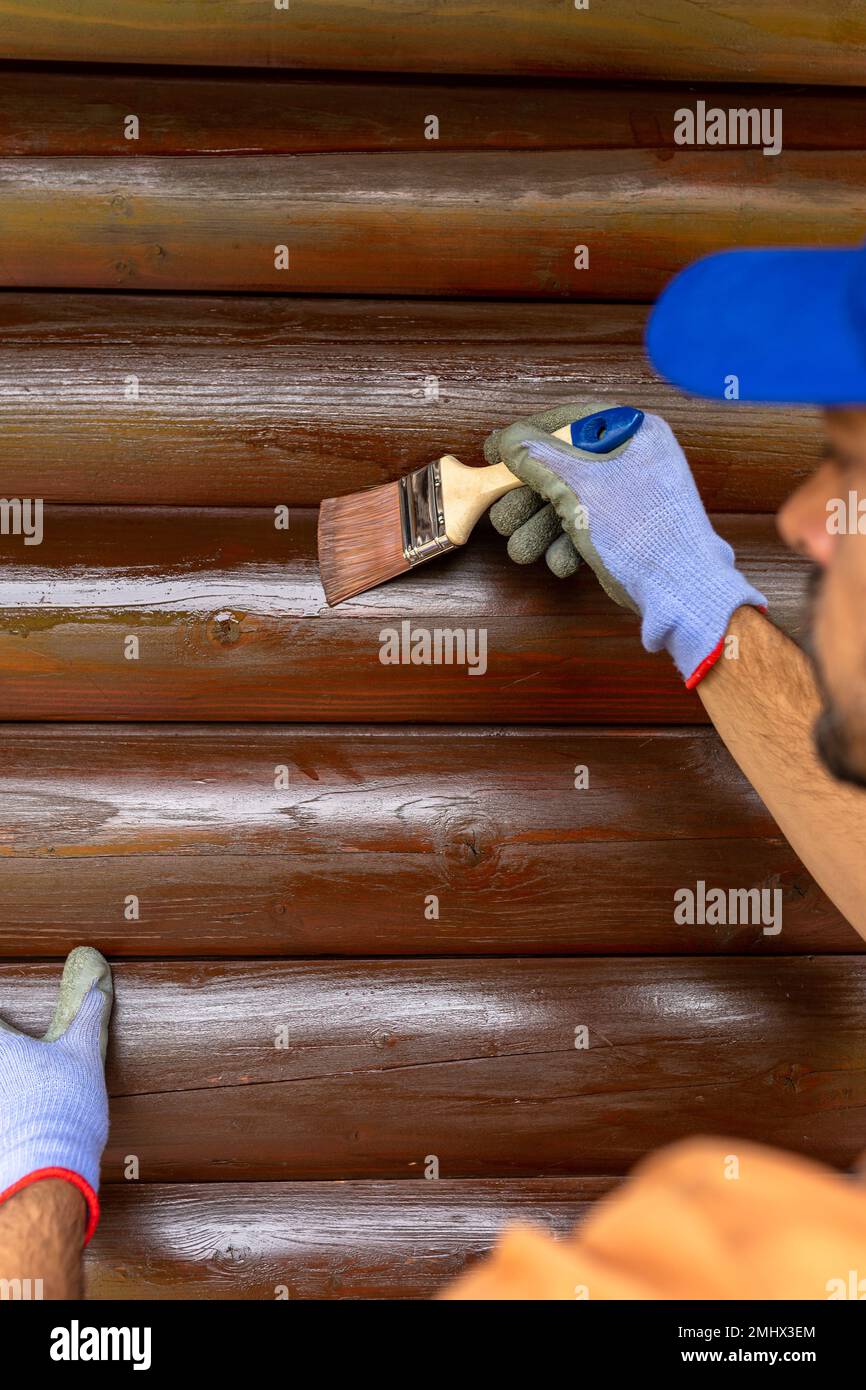 Wooden house maintenance concept. Man staining wall siding trunk Stock