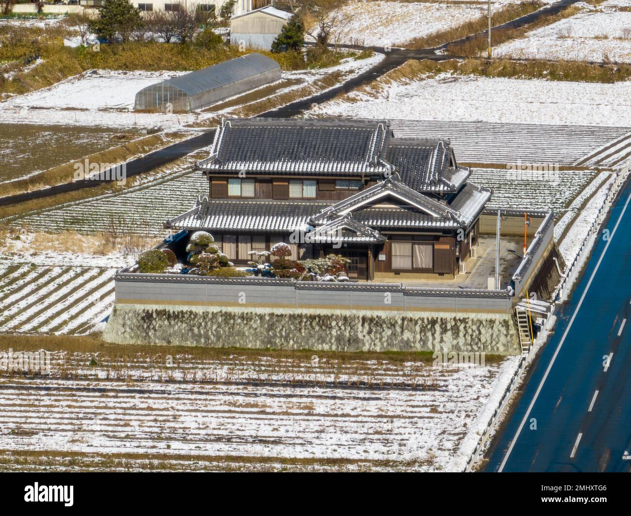Large traditional Japanese farmhouse by snow covered rice fields and road Stock Photo