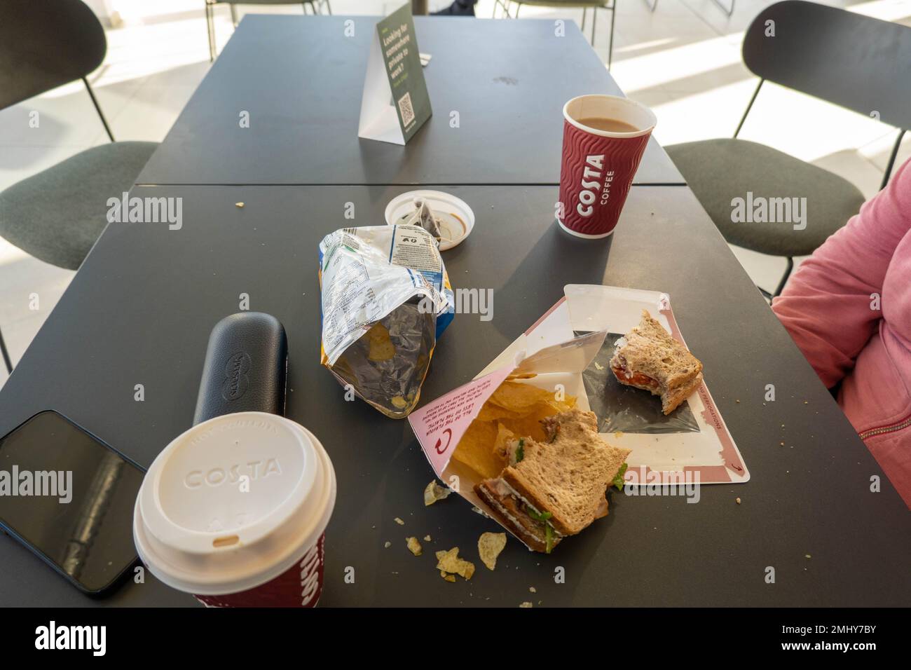 Table at a Costa coffee shop with half eaten sandwich, empty crisp packet   and cup of coffee Stock Photo