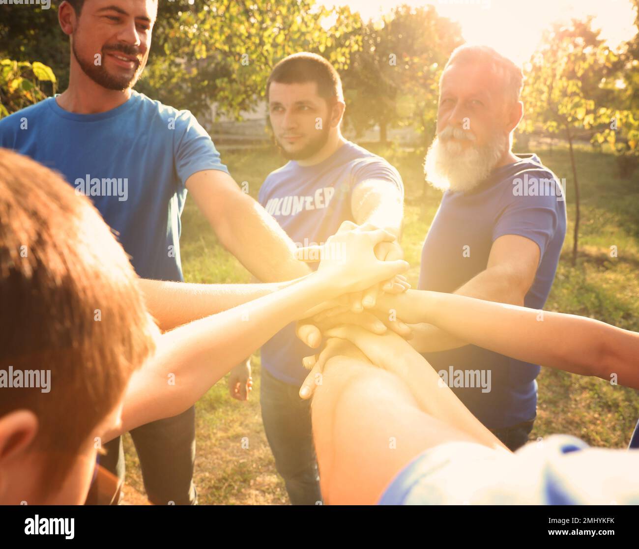 Group of volunteers joining hands together outdoors on sunny day Stock Photo