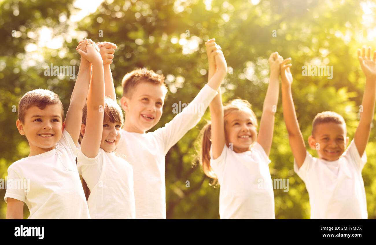 Group of children holding hands up in park on sunny day. Volunteering with kids Stock Photo