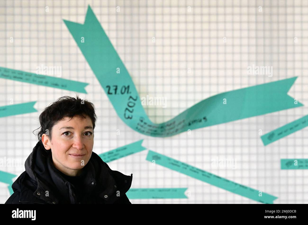 27 January 2023, Brandenburg, Oranienburg: The Berlin artist Susanne Quehenberger stands in the interior of 'Station Z' of the Sachsenhausen Memorial and Museum in front of a wall with labeled adhesive tapes. During a joint commemoration event of the Brandenburg State Parliament and the memorial site, the cultural scientist's tape art action with the question 'Why do you remember today?' was performed for the first time instead of laying a wreath. In addition to the visitors to the memorial, more than 90 people had responded to the memorial's call and had previously shared their contributions Stock Photo