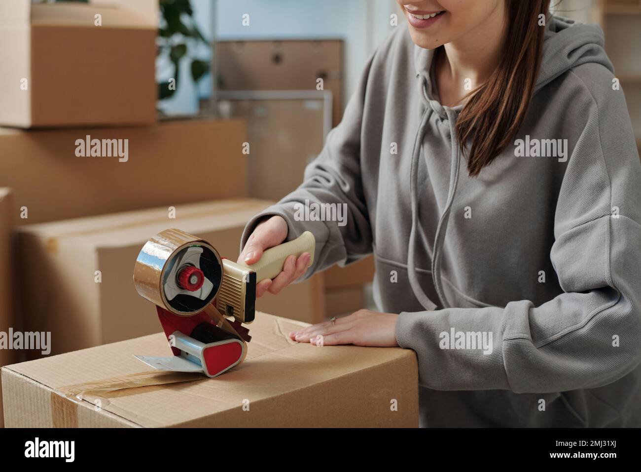 Closeup of young girl using adhesive tape to pack things in cardboard