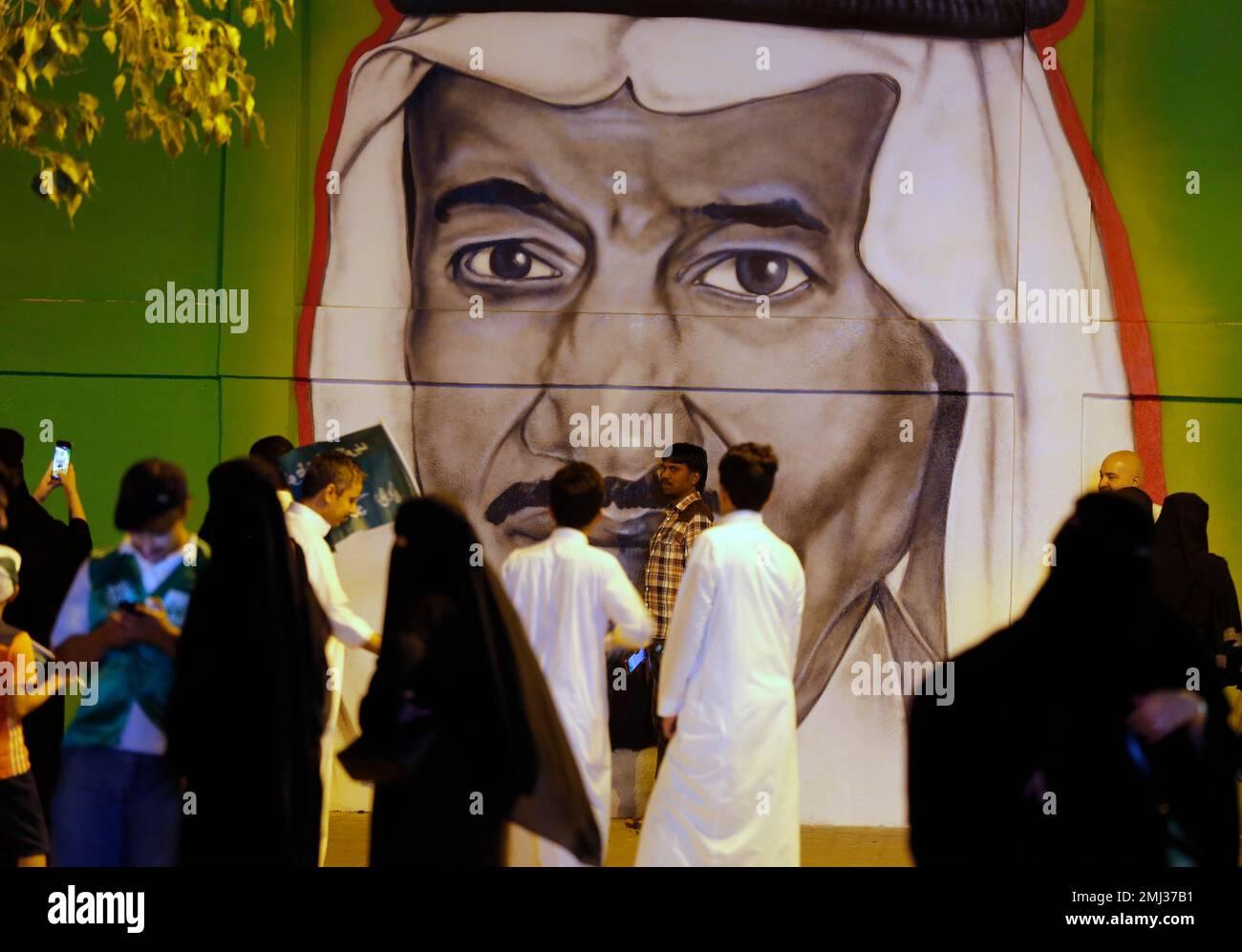 People pos§e for pictures in front of graffiti showing Saudi King ...