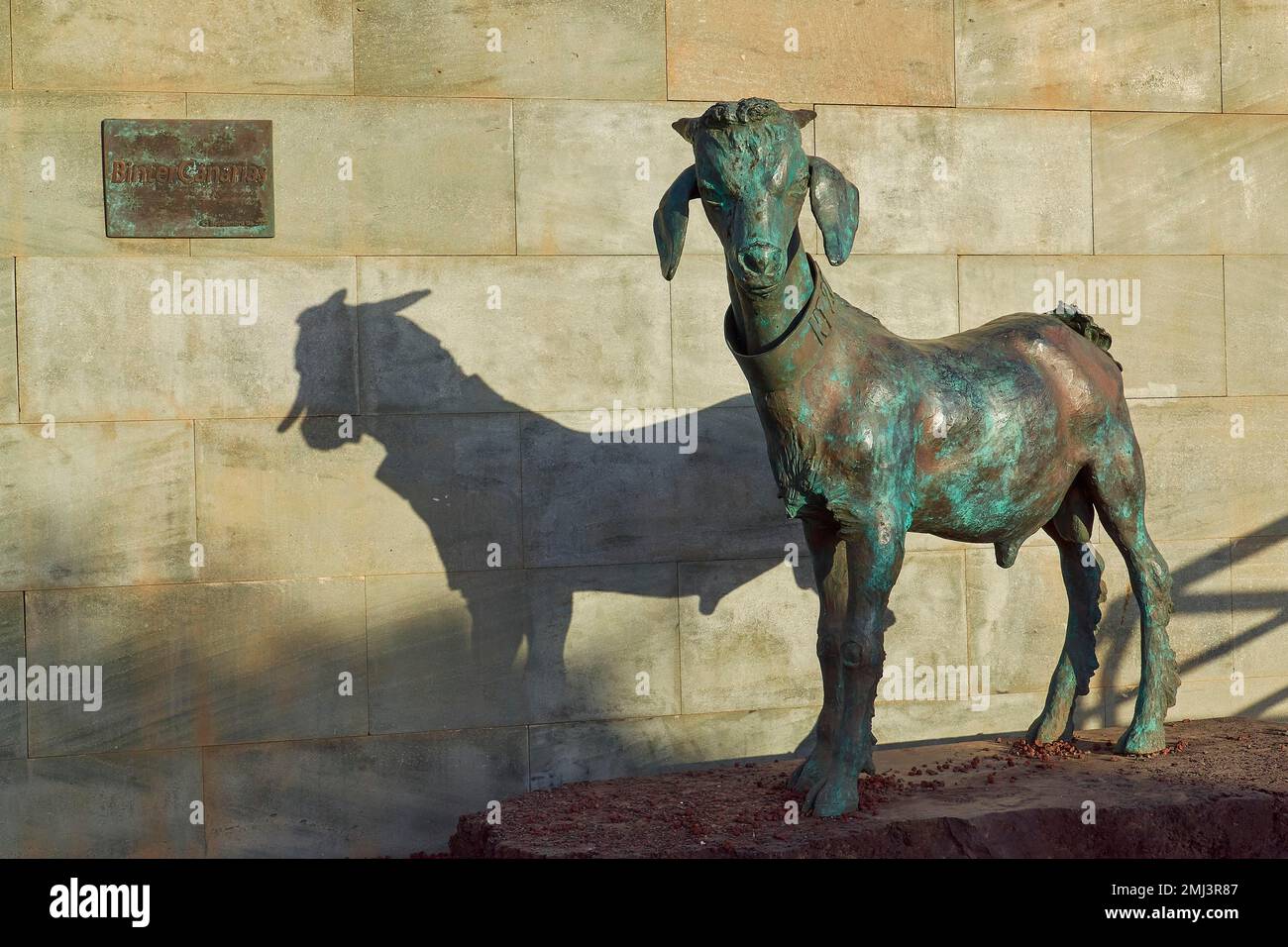Bronze statue of a goat, shadow on the stone wall, harbour, capital
