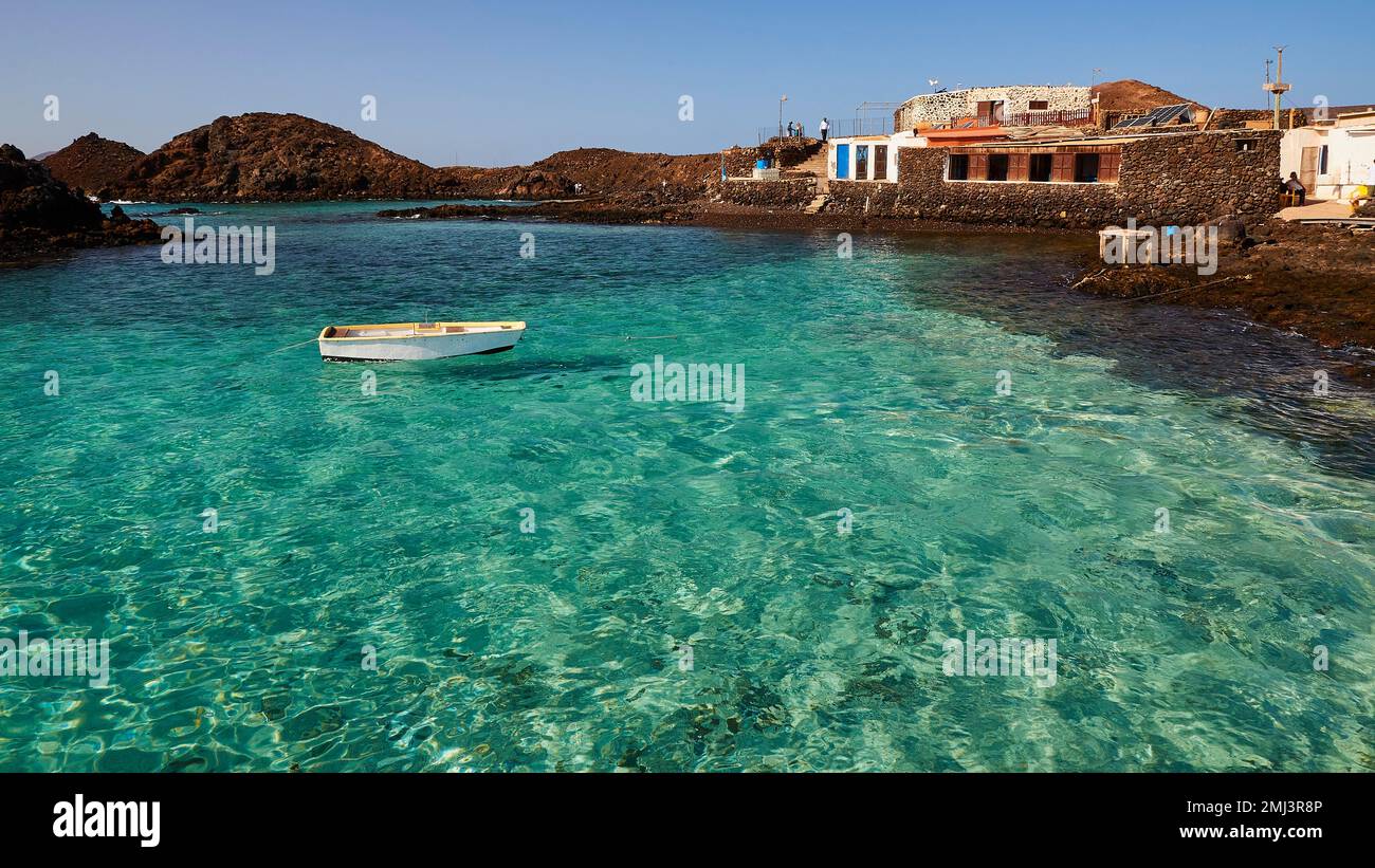 Harbour basin, boat floating on the water, crystal clear green sea, harbour building, north, Los Lobos Island, nature reserve, blue cloudless sky Stock Photo