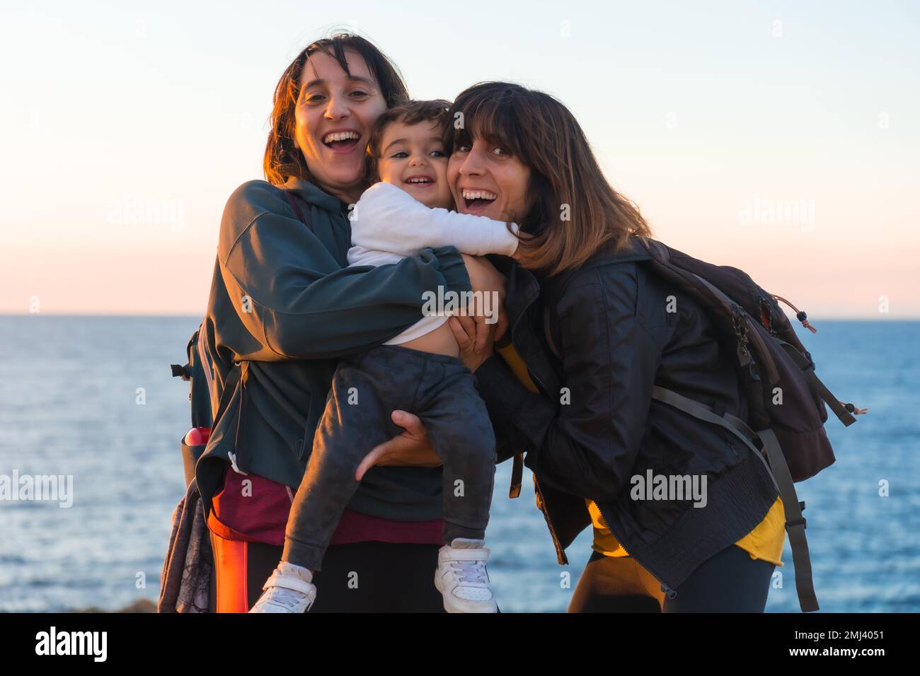 Aunt of the child and mother hugging with him child on the coast by the sea at sunset Stock Photo