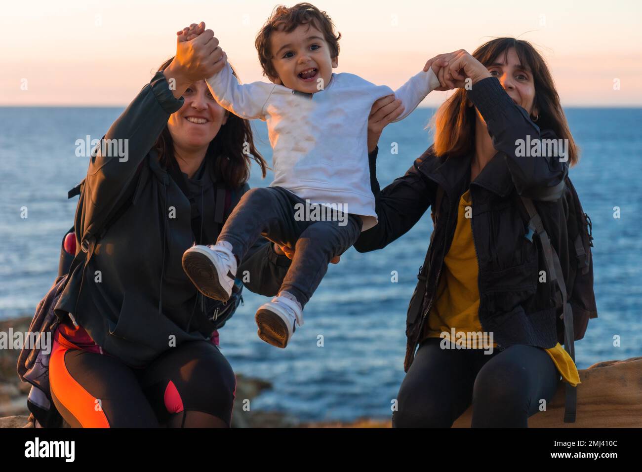 Aunt of the child and mother playing with him child on the coast by the sea at sunset Stock Photo