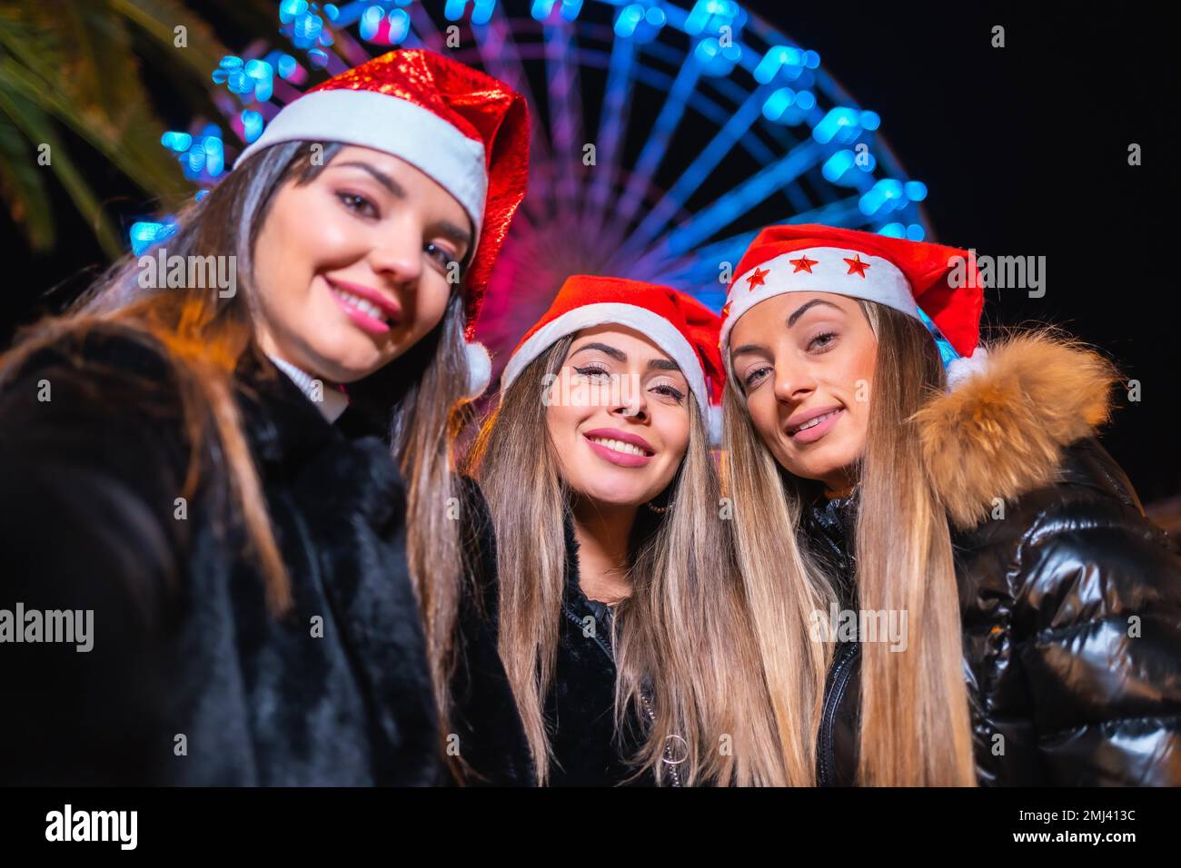 Christmas in the city at night, decoration in winter. Friends on an illuminated Ferris wheel taking a selfie Stock Photo