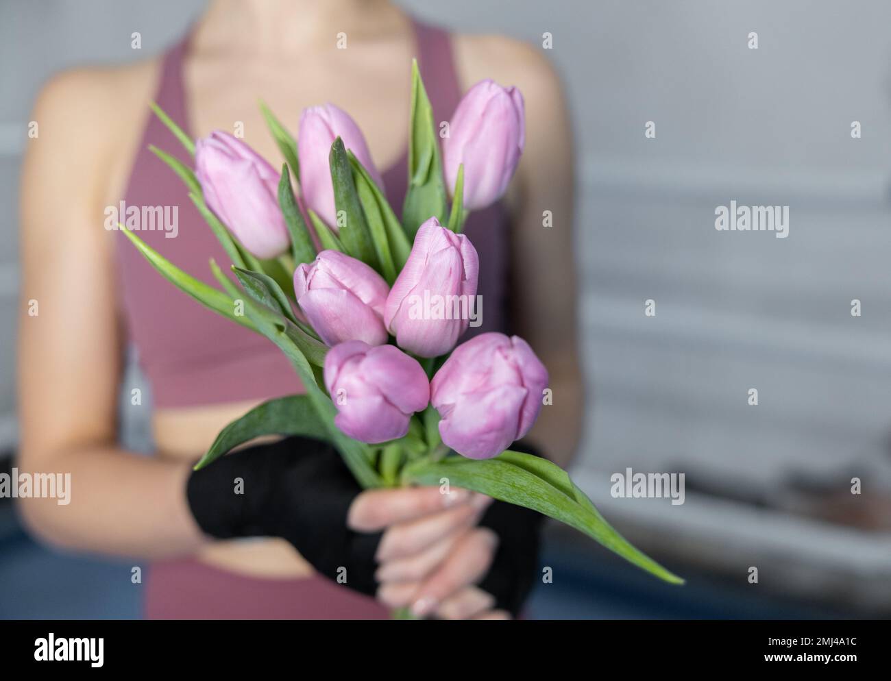 Girl boxer with bandaged hands holds seven tulips, women's sport, gentle boxing Stock Photo