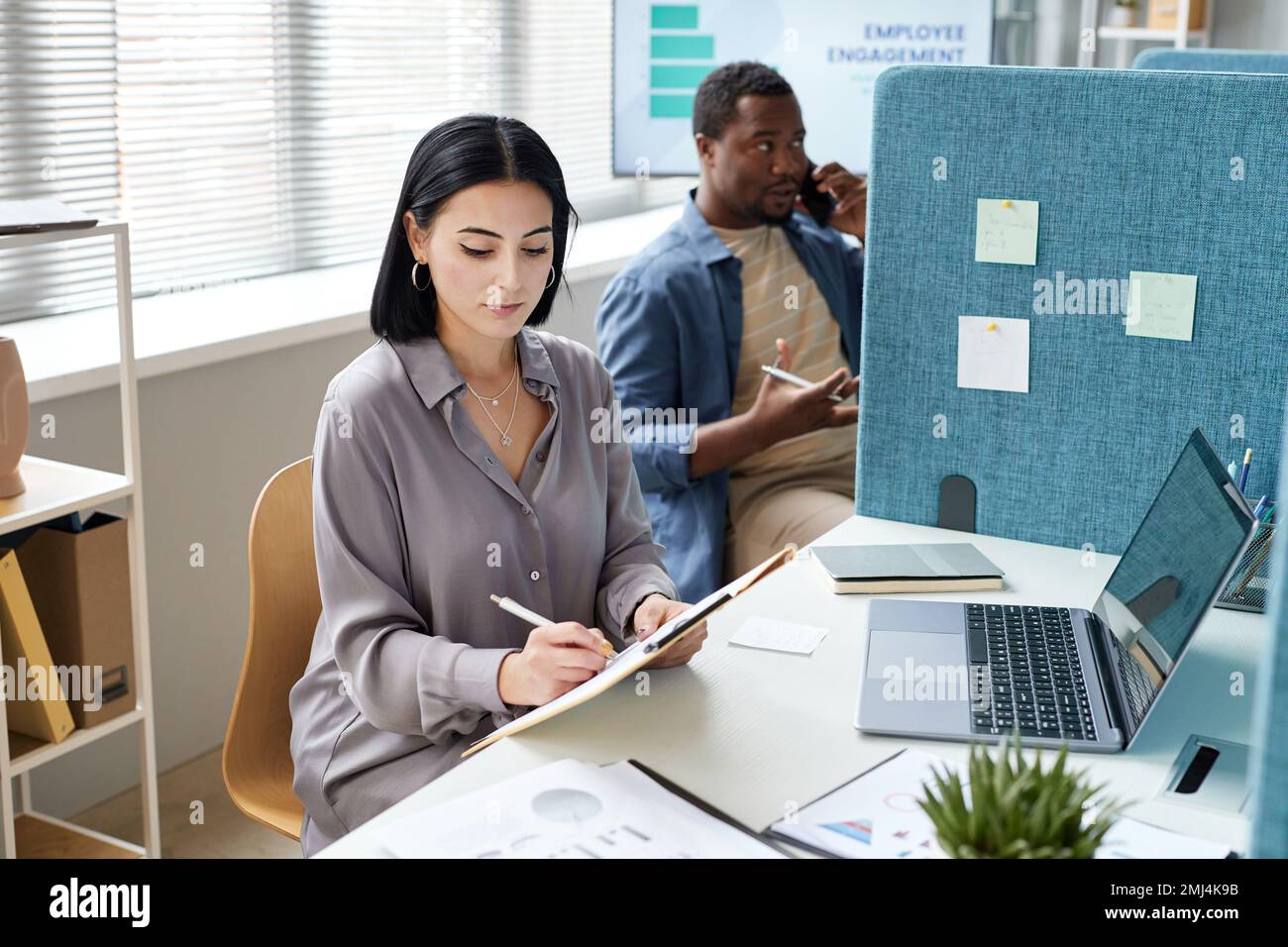 Portrait of young businesswoman writing on clipboard while working in ...