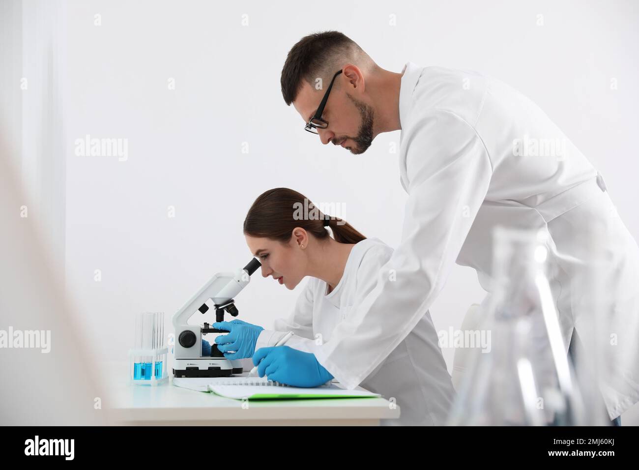 Scientist using microscope at table and colleague in laboratory ...