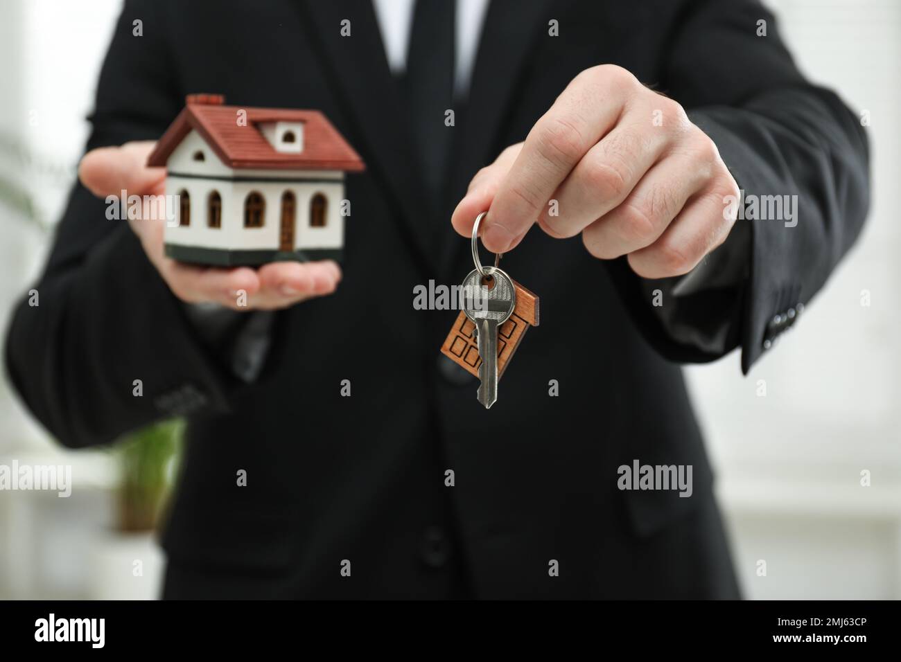 Real estate agent holding house model and key indoors, closeup Stock ...