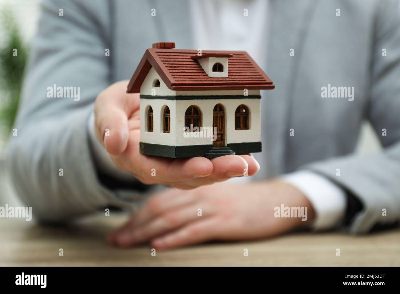 Real estate agent holding house model at wooden table, closeup Stock ...