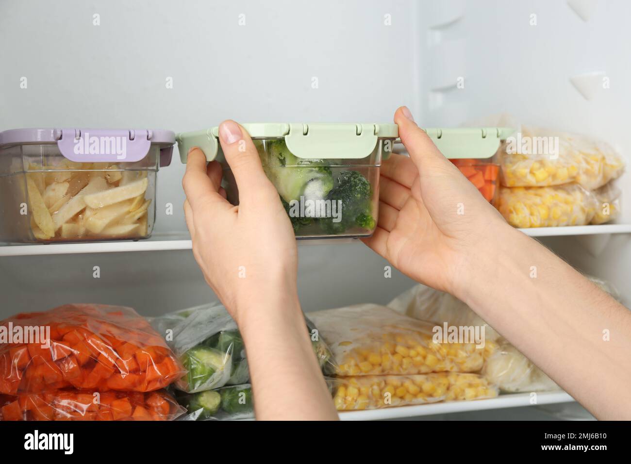 https://c8.alamy.com/comp/2MJ6B10/woman-putting-container-with-broccoli-in-refrigerator-with-frozen-vegetables-closeup-2MJ6B10.jpg