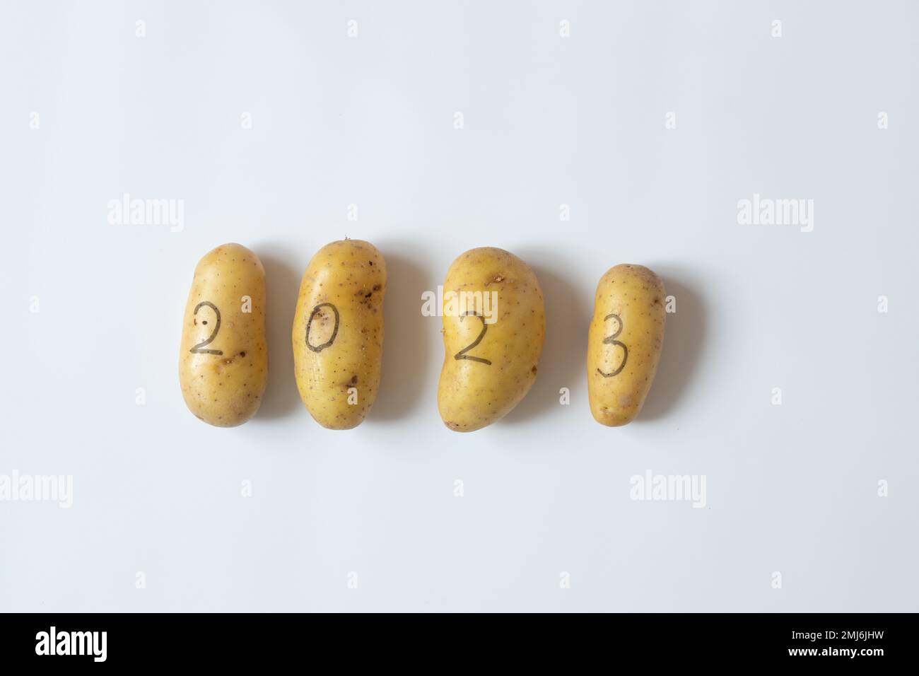 Four raw potatoes with the numbers 2023 written with a black felt-tip pen lie on a white background, vegetables in the new year Stock Photo