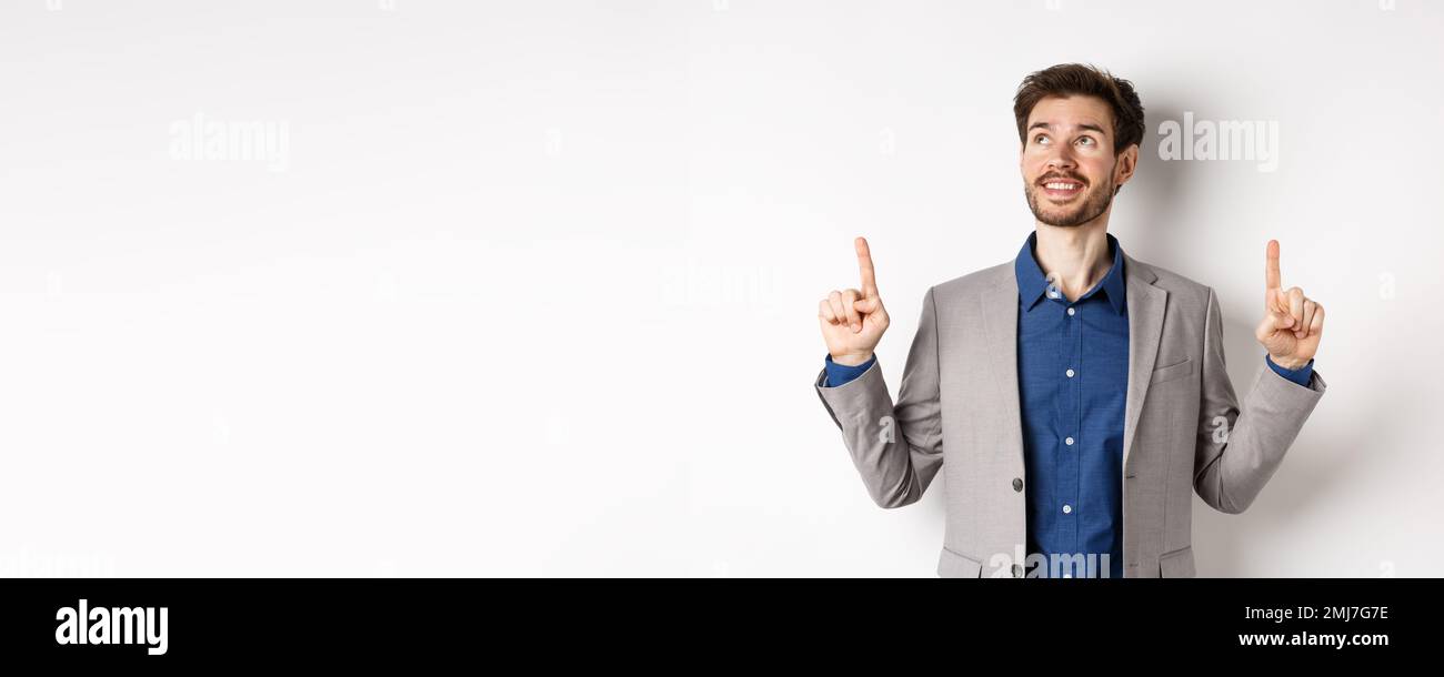 Dreamy smiling male manager in suit pointing and looking up, happy face ...