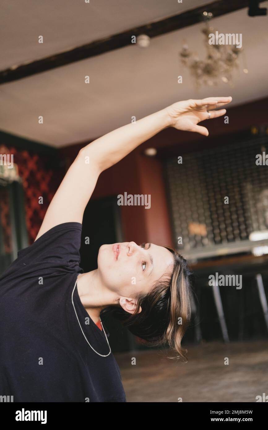 Close-up photo of a female new yoga teacher doing a seated side body stretch wearing a black t-shirt indoors Stock Photo