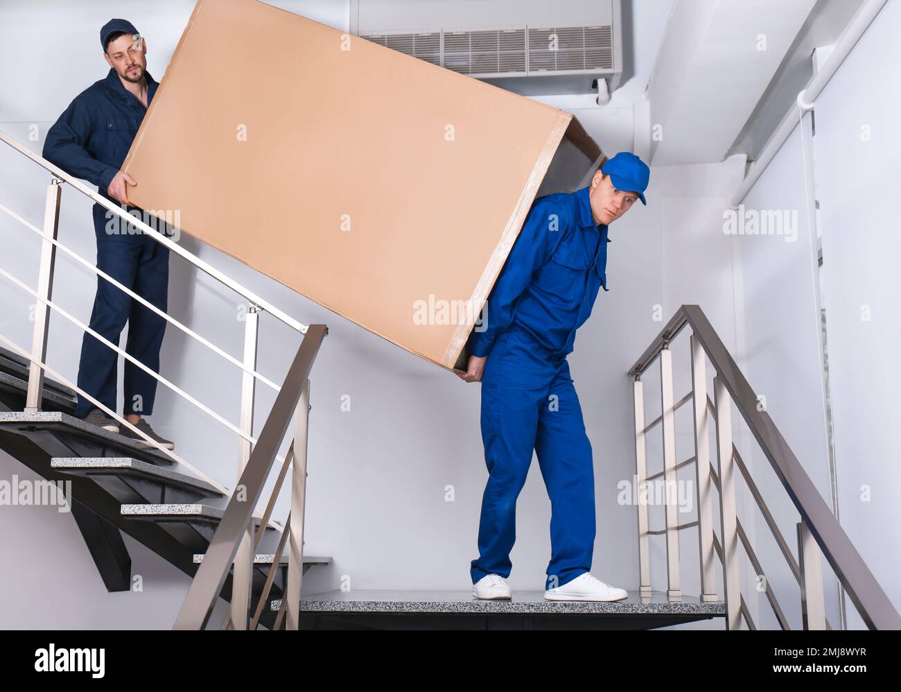 Professional workers carrying refrigerator on stairs indoors Stock