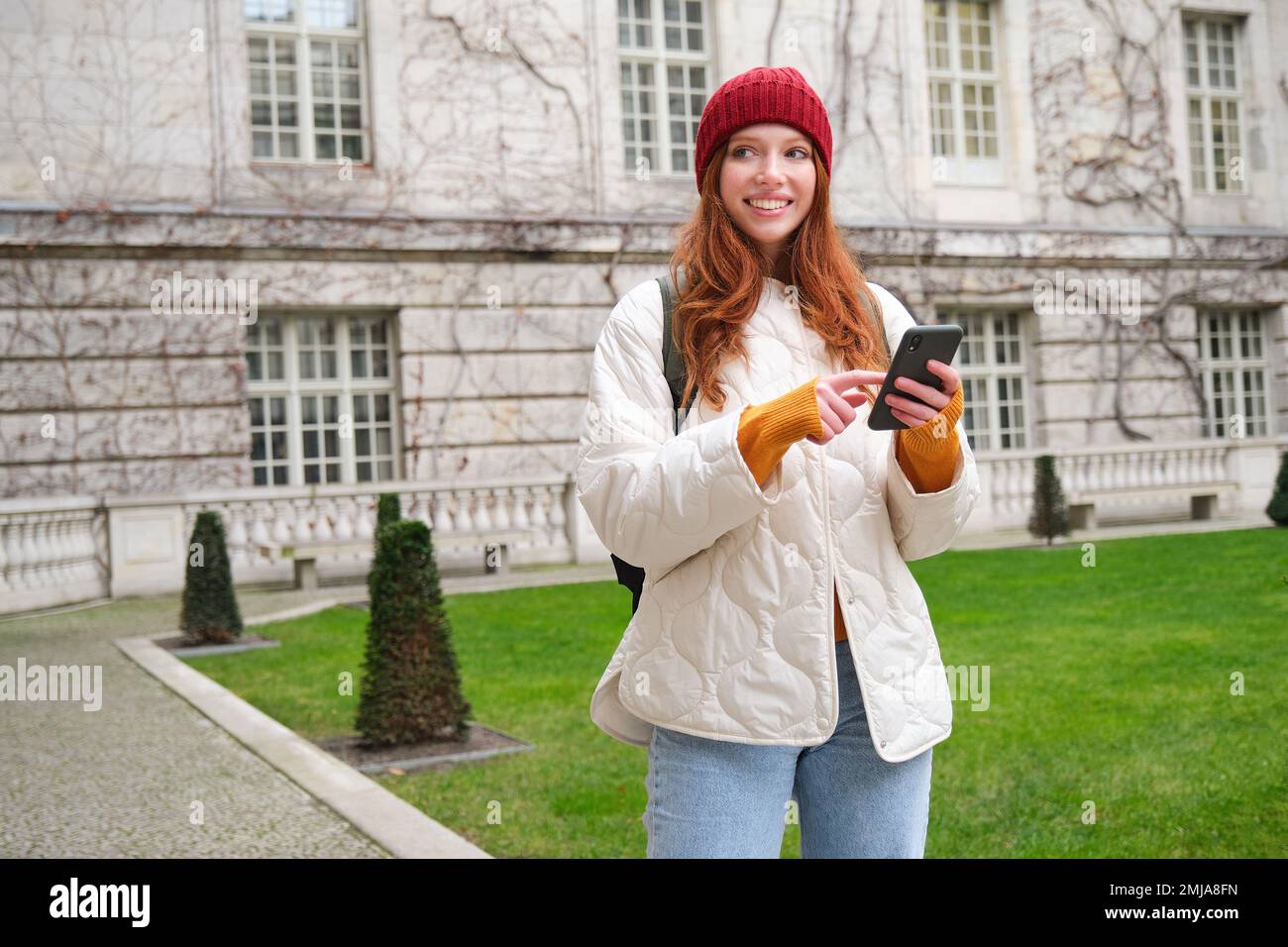 Portrait of girl tourist, wonders around city with smartphone map application, holding mobile phone and smiling, looking up info in internet Stock Photo
