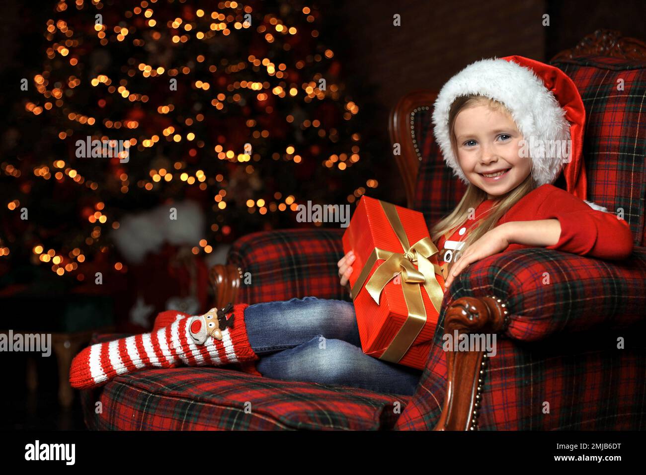 Cute little child with Christmas gift sitting in armchair at home Stock Photo