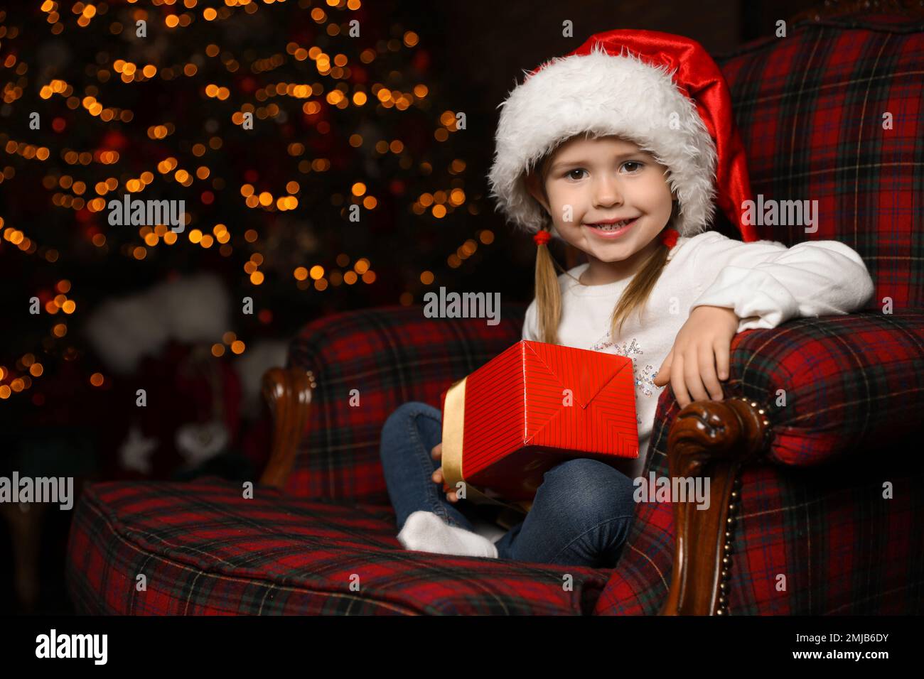 Cute little child with Christmas gift sitting in armchair at home Stock Photo