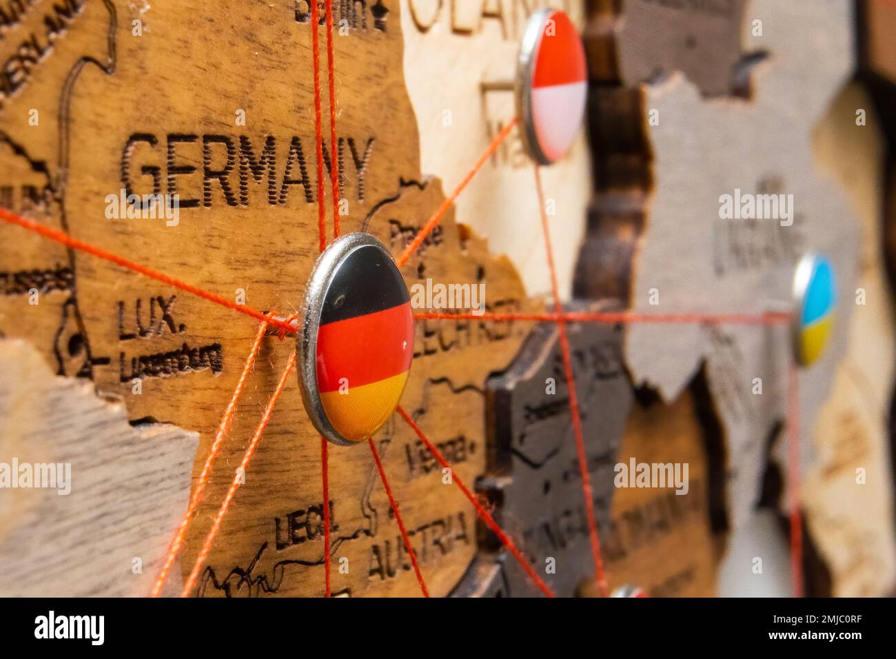 Germany, Poland and Ukraine flags on the pushpin with red thread showed the paths of movement or areas of influence in the global economy on the wooden map. Planning of traveling or logistic concept. Help in the war against Russia.  Stock Photo