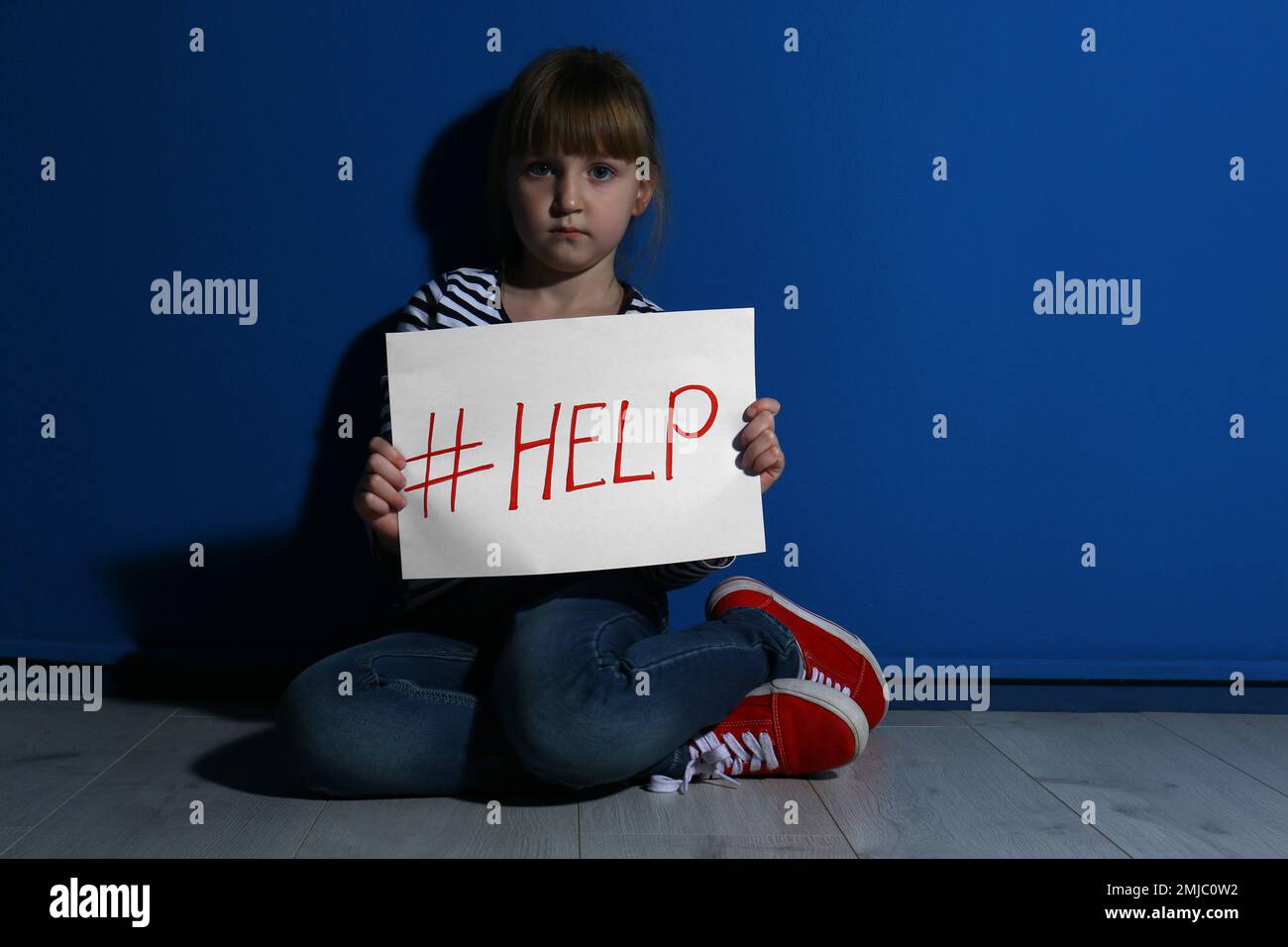 Abused little girl with hashtag HELP near blue wall. Domestic violence