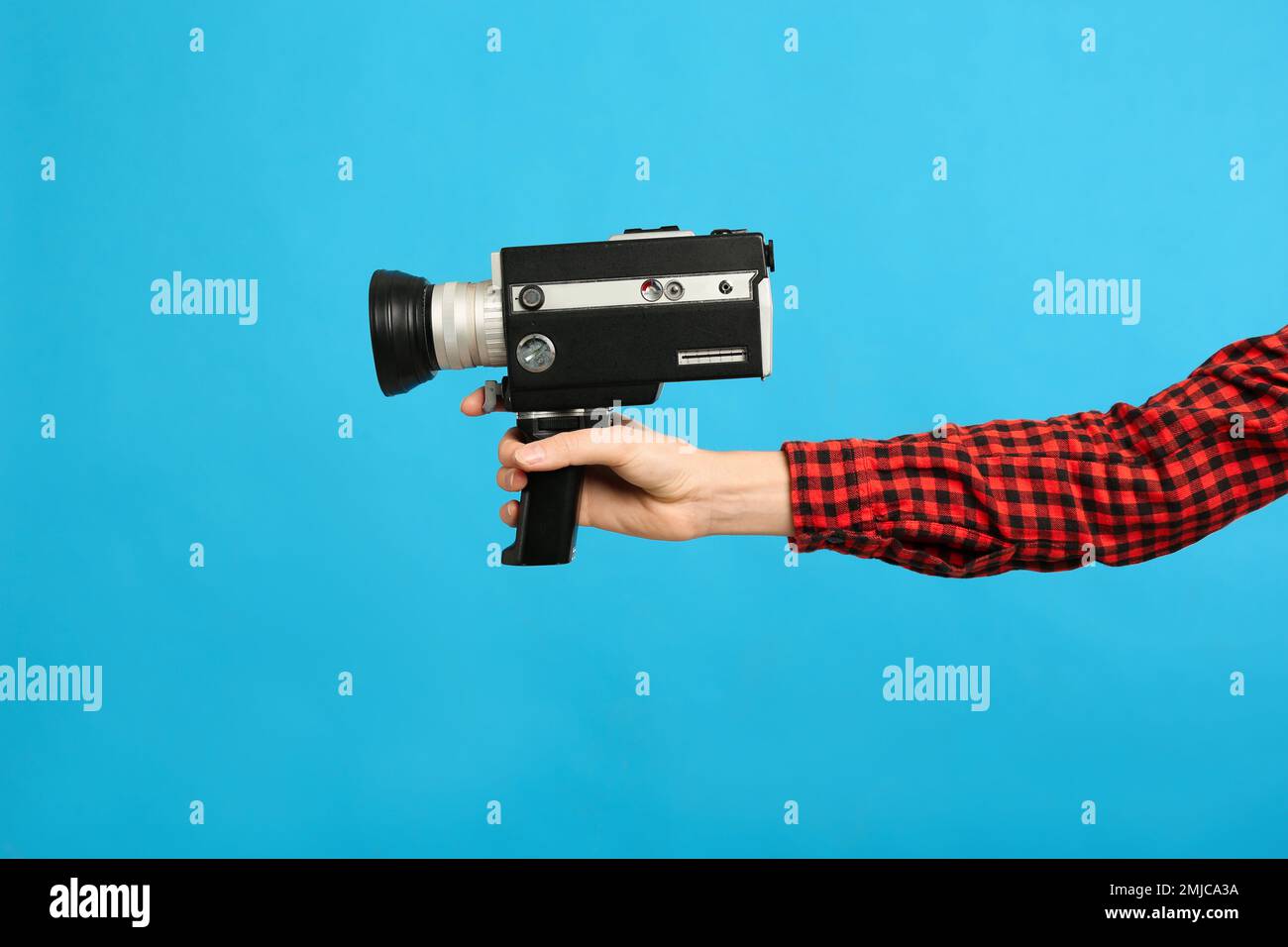 Woman with vintage video camera on light blue background, closeup of