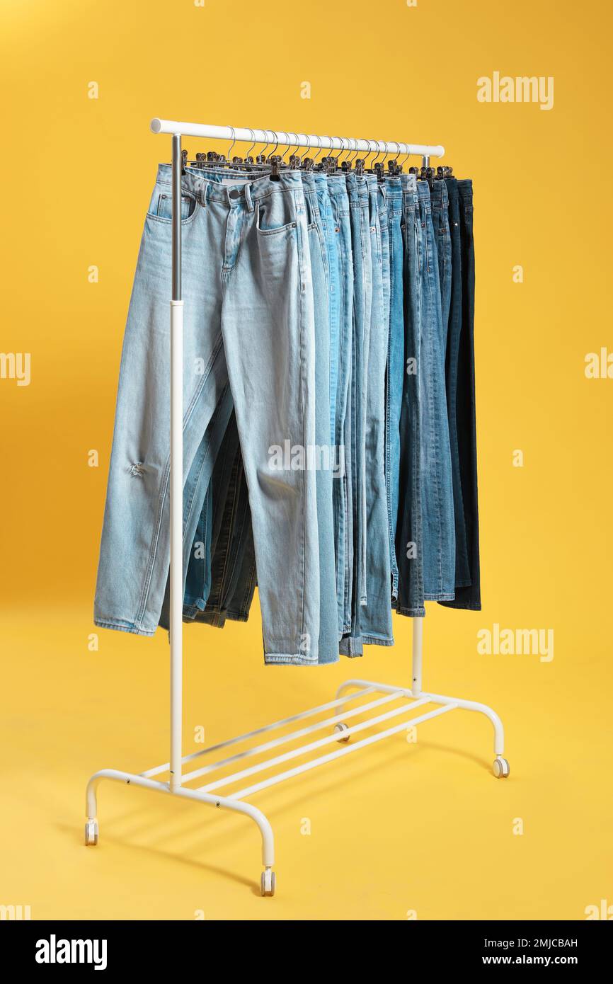 Rack with different jeans on yellow background Stock Photo - Alamy
