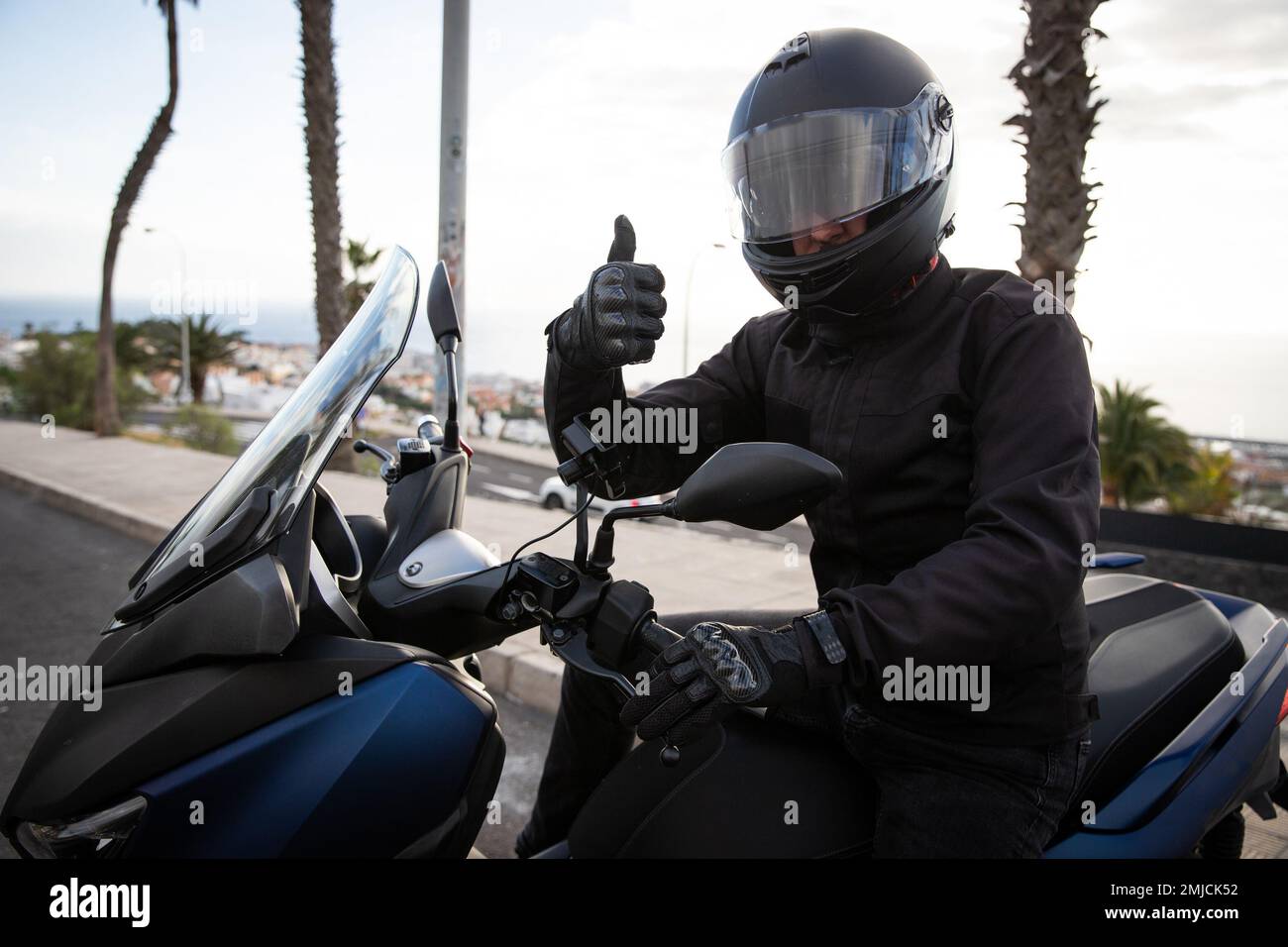 A motorcyclist on his motorcycle gives the thumbs up, happy motorcycle enthusiast. Stock Photo