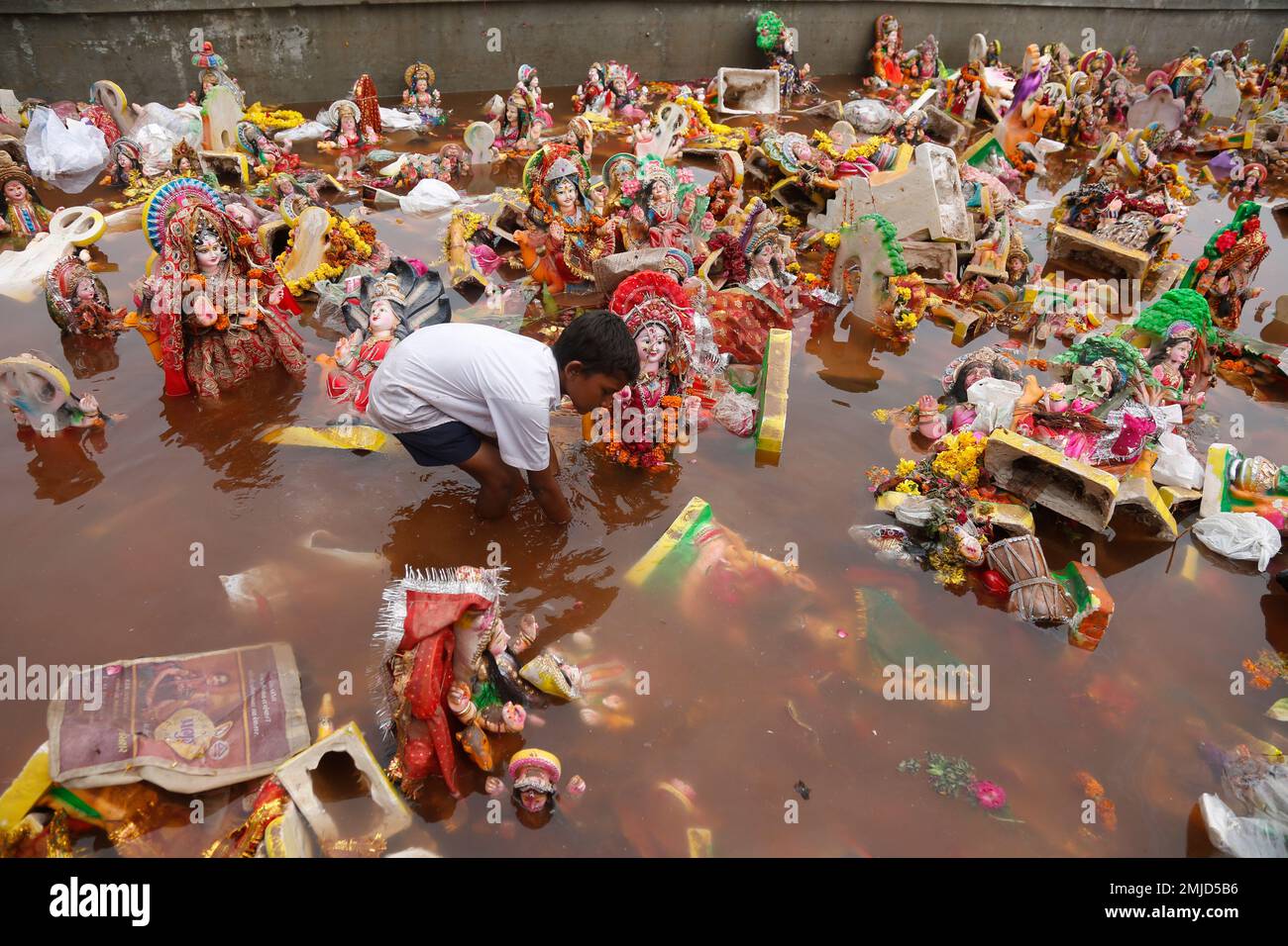 An Indian boy searches for reusable items amid idols of Hindu goddess ...
