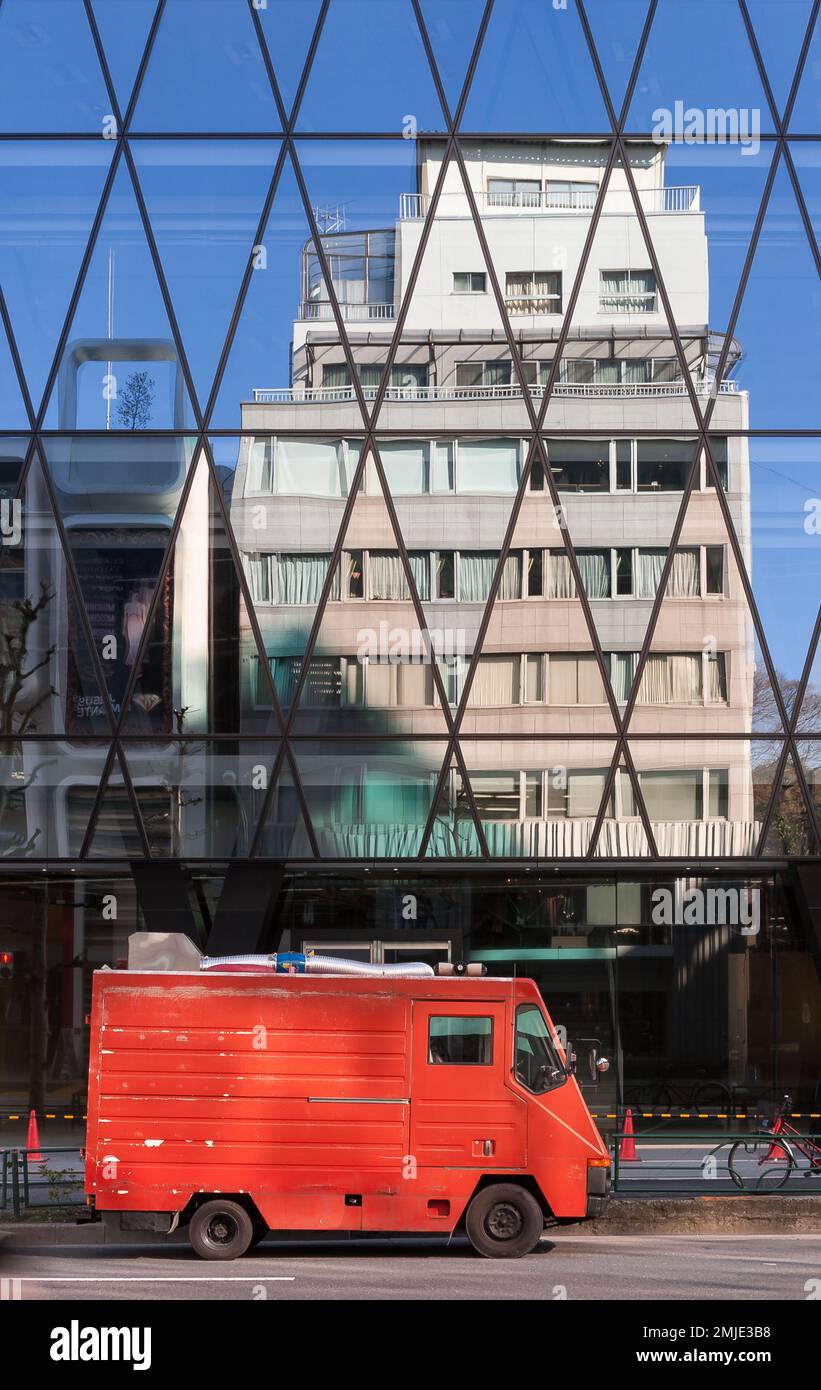 An old red van in a street in Shibuya with buildings reflected in a glass fronted office building above, Tokyo, Japan Stock Photo