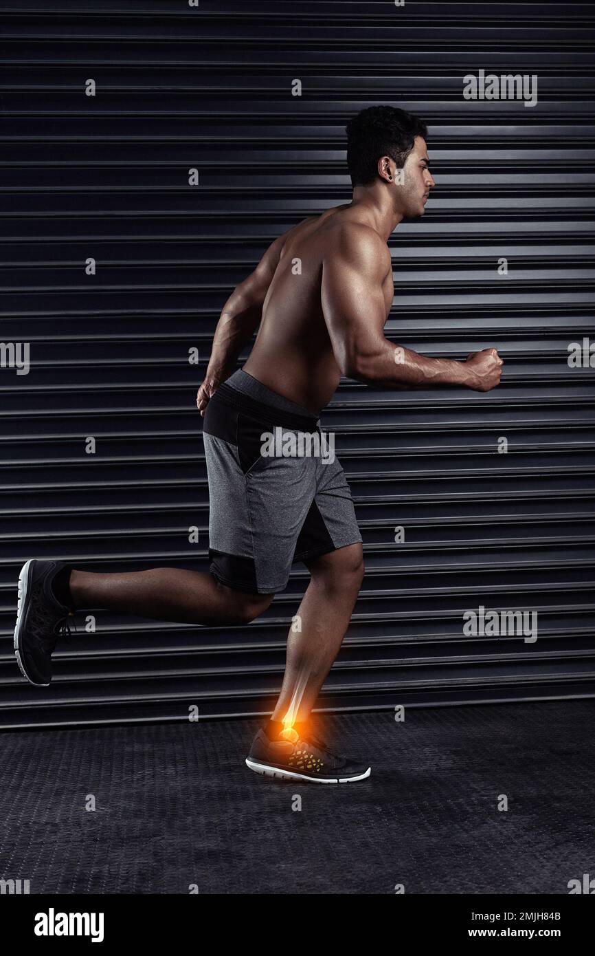 Feeling the pressure on his ankle. Full length shot of a handsome young man running against a dark background. Stock Photo
