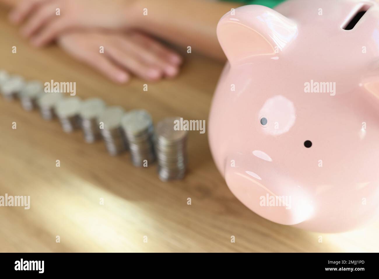 Many stacks of coins of different heights and piggy bank on wooden table. Stock Photo