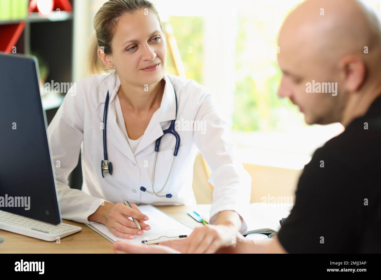 Female doctor listens to her patient while sitting at office desk in medical clinic. Stock Photo