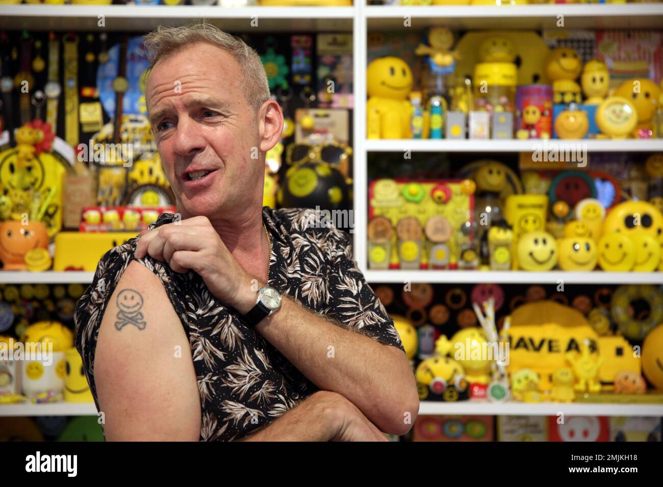 Norman Cook, aka Fat Boy Slim, shows his tattoo in front of his collection of objects featuring the smiley face symbol on shelves at the Underdogs Gallery in Lisbon, Friday, June 21,
