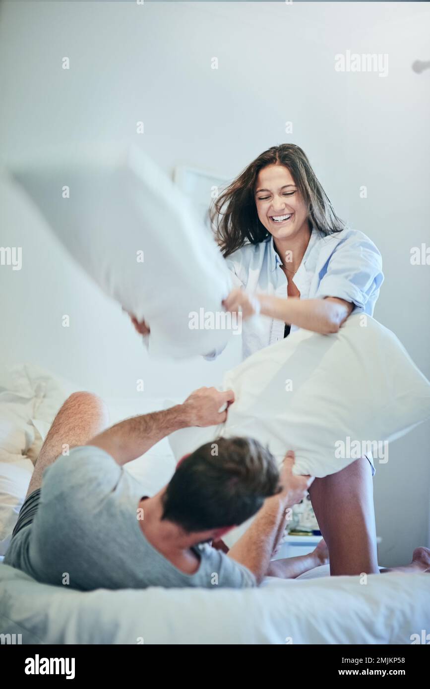 They are such a fun couple. a young couple enjoying a pillow fight in their bedroom. Stock Photo