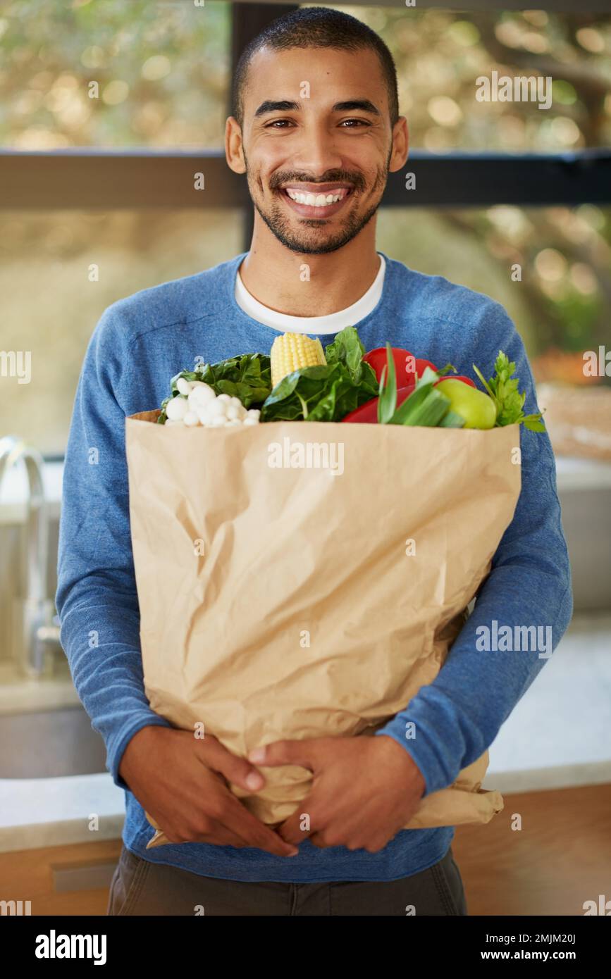 Buy good food and youll eat good food. Portrait of a happy young man holding a bag full of healthy vegetables at home. Stock Photo