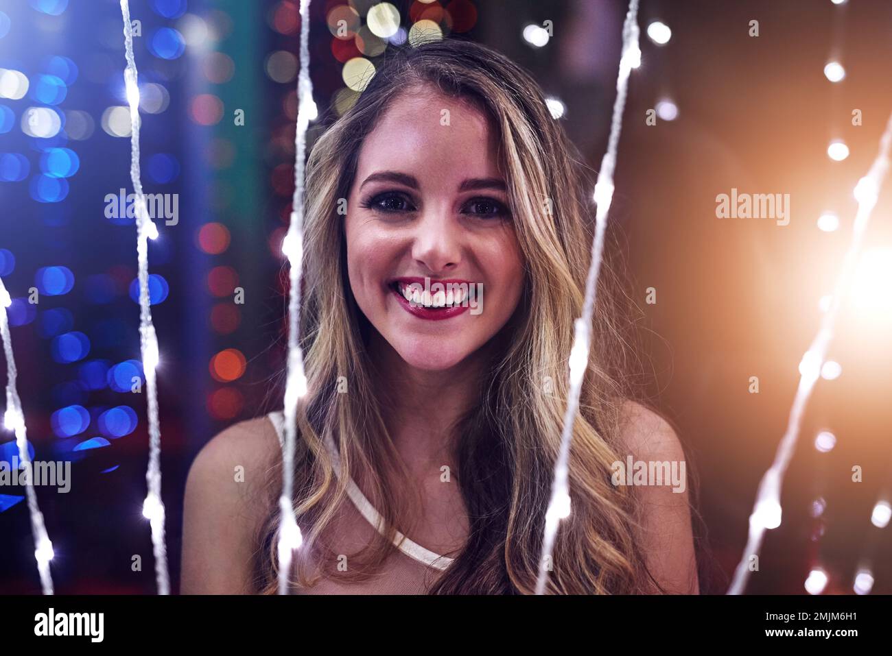 Feeling festive under the party lights. Portrait of a happy young woman playing with string lights in a night club. Stock Photo