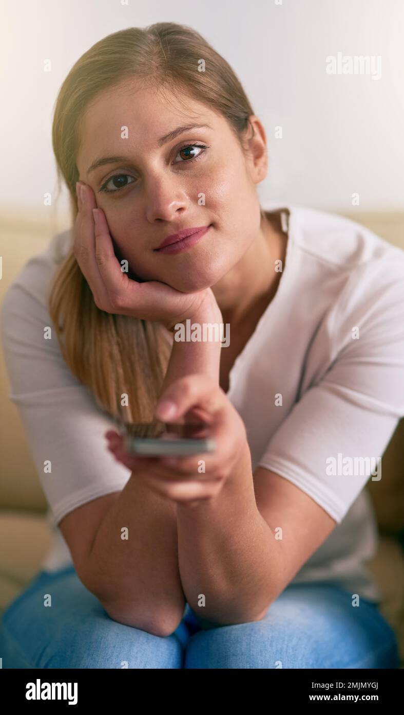 I do relaxation my way. Portrait of a young woman using a remote to change the channels on her TV at home. Stock Photo