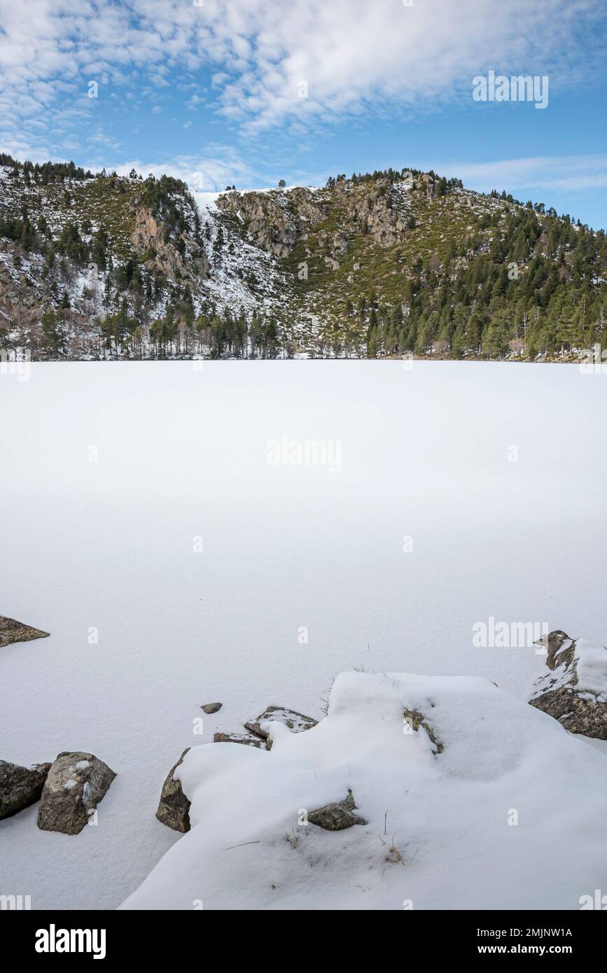 Querigut Pond during the winter months with frozen and snow-covered water, Pyrenees, Ariege, France. Landscape with mountains and snow Stock Photo