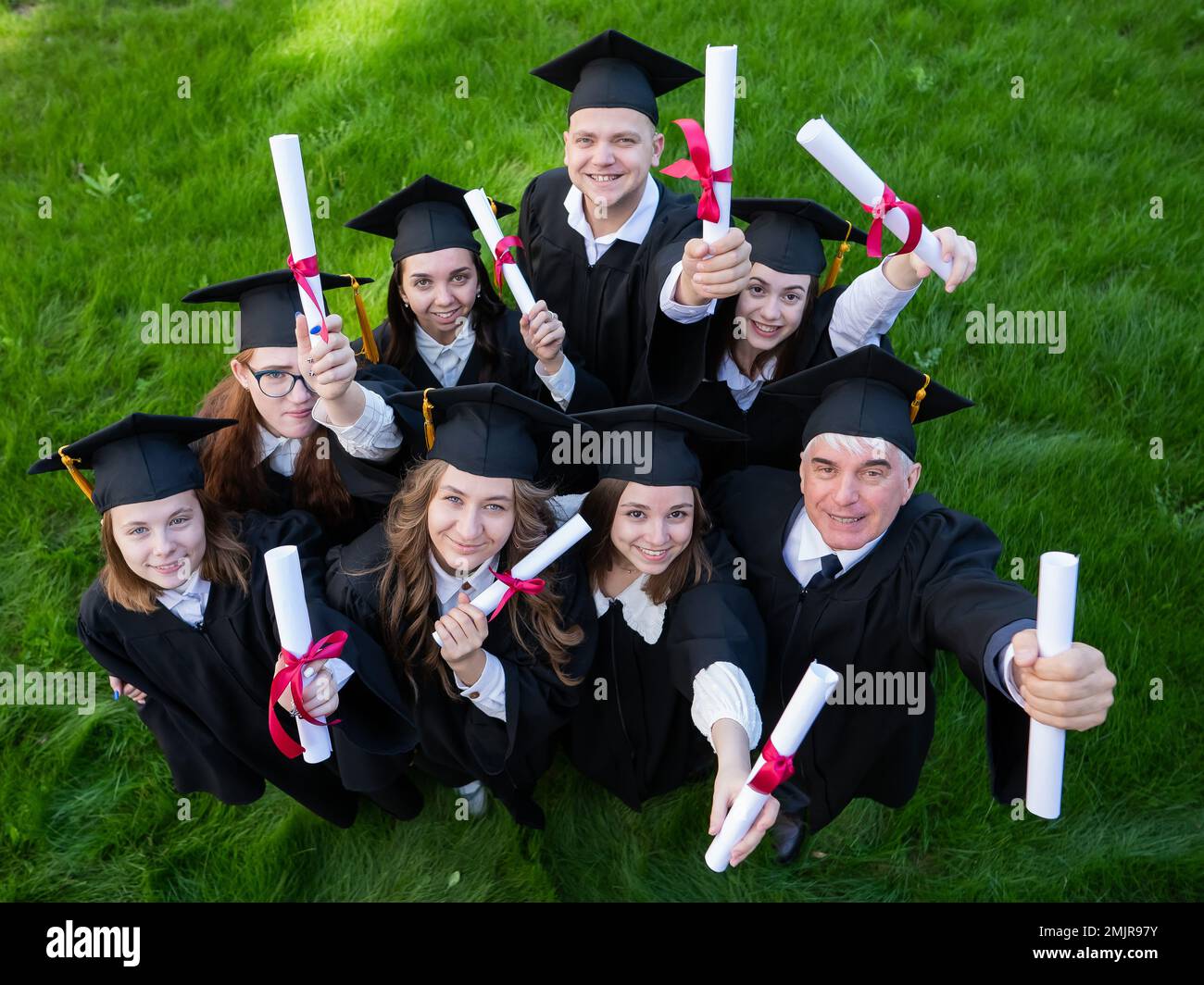 Graduates in robes show off their diplomas outdoors. View from above. Age student. Stock Photo