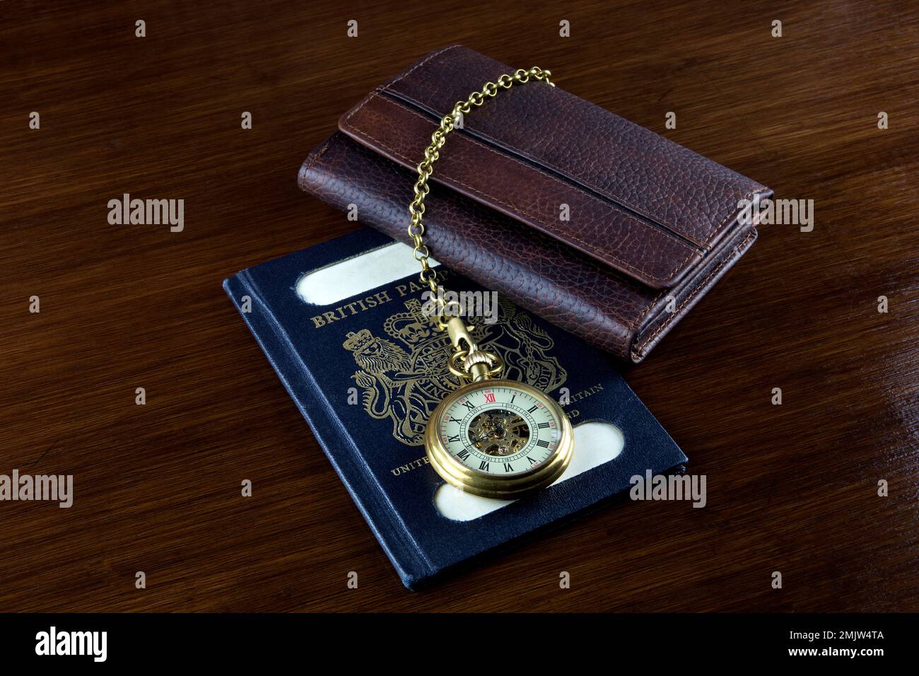 Old pocket watch with leather wallet and vintage UK passport on a wooden table top Stock Photo